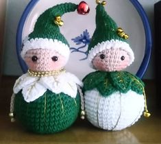 two small crocheted dolls sitting next to each other on a table with a plate in the background