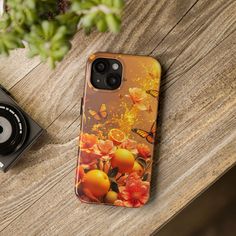 an iphone case sitting on top of a wooden table next to a camera and plant