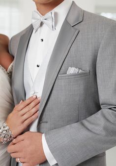 a man in a gray suit and bow tie standing next to a woman wearing a white dress