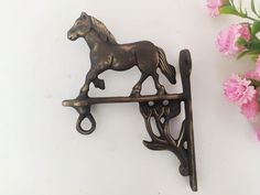 a metal horse on a hook next to pink flowers