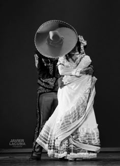 a man and woman in traditional mexican garb performing a dance on stage with a large hat over their head