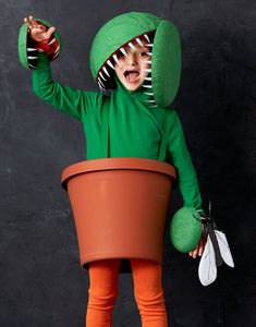 a child in a green dinosaur costume holding a potted plant with its mouth open