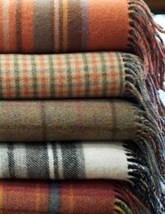 four plaid blankets stacked on top of each other in different colors and patterns, all folded neatly