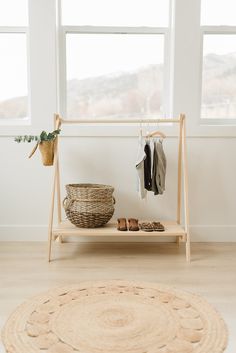 a wooden shelf with clothes and shoes on it in front of a window next to a rug