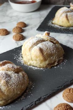 three pastries sitting on top of black slate trays covered in powdered sugar