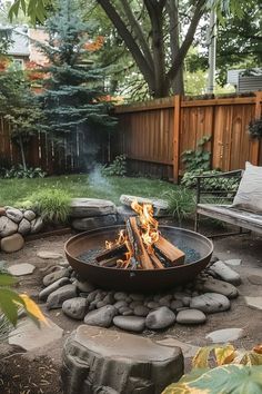 an outdoor fire pit surrounded by rocks and gravel in a backyard area with trees, bushes, and benches