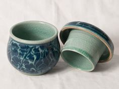 two green and blue vases sitting on top of a white sheet