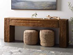 a wooden bench sitting next to two baskets on top of a rug in front of a painting