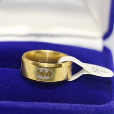 a gold ring with a batman symbol on it in a blue velvet box and white plastic spoon