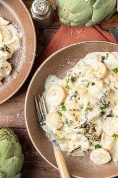 two brown bowls filled with food next to artichokes on a wooden table