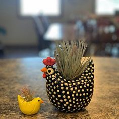 a small yellow rubber duck sitting next to a ceramic chicken planter on a counter