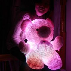 a woman holding a pink teddy bear in her hands with the light shining on it