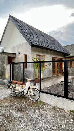 a moped parked in front of a house behind a black metal fence and gate