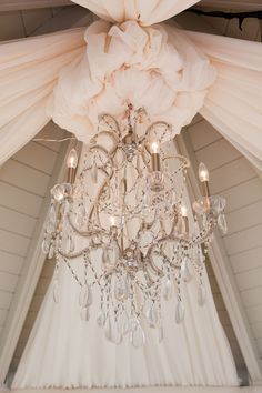 a chandelier hanging from the ceiling in a white room with sheer drapes