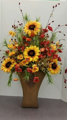 a vase with sunflowers and other flowers in it on the floor next to a wall