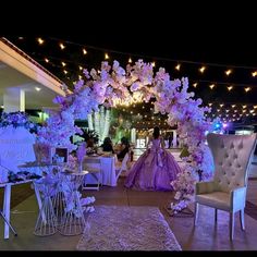 an outdoor wedding venue decorated with purple flowers and white chairs, surrounded by fairy lights