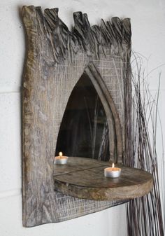 two candles are lit in front of a mirror on a wooden shelf next to some dry grass