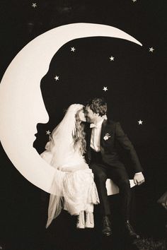 a black and white photo of a bride and groom kissing in front of the moon