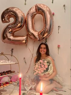 a woman sitting in front of a table with balloons and flowers on it, holding a bouquet