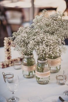 three mason jars filled with baby's breath flowers on top of a white table cloth