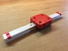 a red and white plastic object sitting on top of a wooden table next to a ruler