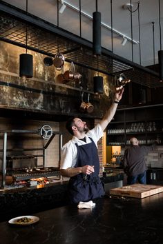 a man standing in front of a counter with pots and pans hanging from the ceiling