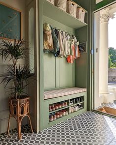 a room with a bench, potted plant and clothes hanging on the door hangers