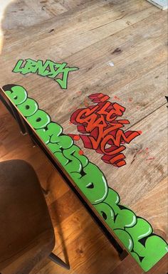 a skateboard with graffiti on it sitting on top of a wooden table next to a chair