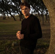 a young man standing next to a tree