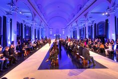 people are sitting on benches in the middle of a large room with blue lights and chandeliers