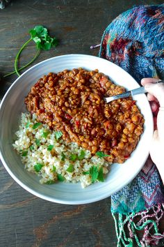 a person holding a spoon over a bowl of beans and rice on a wooden table