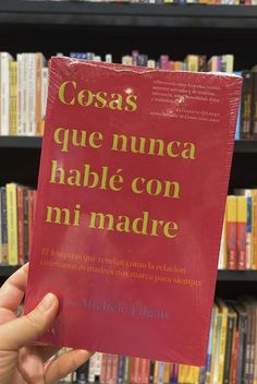 a person holding up a red book in front of a bookshelf filled with books