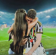 two people embracing each other in front of a soccer field with lights on the sidelines