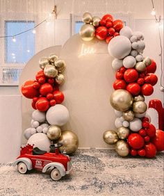 a red firetruck is parked in front of a balloon arch with silver and gold balloons