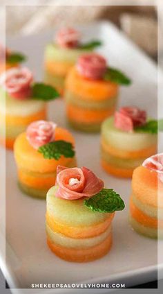 small desserts are arranged on a white plate with green leaves and pink flowers in the middle