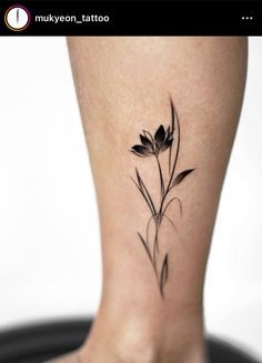 a black and white photo of a flower tattoo on the leg, with leaves coming out of it