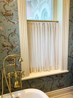 a bath tub sitting under a window next to a curtained window with birds on it