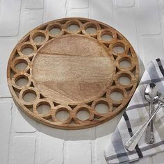 a wooden cutting board with holes in the middle and spoons next to it on a white brick wall