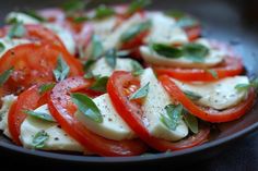 tomatoes and mozzarella on a black plate with basil sprinkled on top