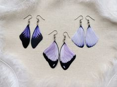 three pairs of purple and black earrings on a white furnishce background with feathers