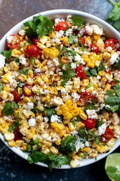 a bowl filled with corn, tomatoes and feta cheese on top of a table