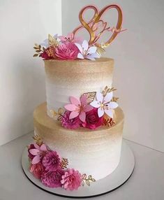 a three tiered cake with pink flowers and gold numbers on it's side