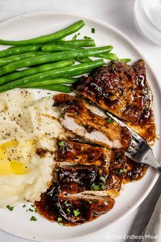 a white plate topped with meat, mashed potatoes and green beans