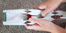 two hands are holding an origami model that looks like a rocket ship with paper on it