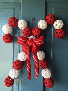 a red and white christmas wreath hanging on the front door with balls attached to it