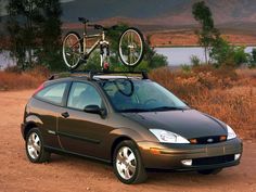 a car with a bike on top of it's roof rack in front of a lake