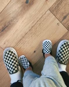 a person wearing black and white checkered shoes standing on a wooden floor with their legs crossed