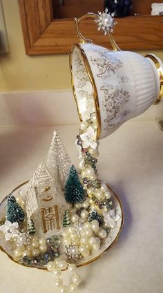 a tea cup is filled with pearls and christmas trees on a saucer that sits on a table