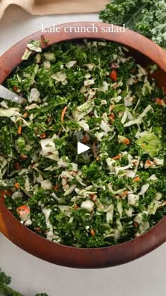 a wooden bowl filled with green vegetables on top of a white tablecloth next to carrots and kale