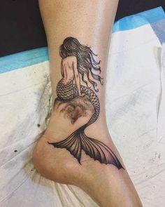 a woman's foot with a tattoo of a mermaid sitting on top of it